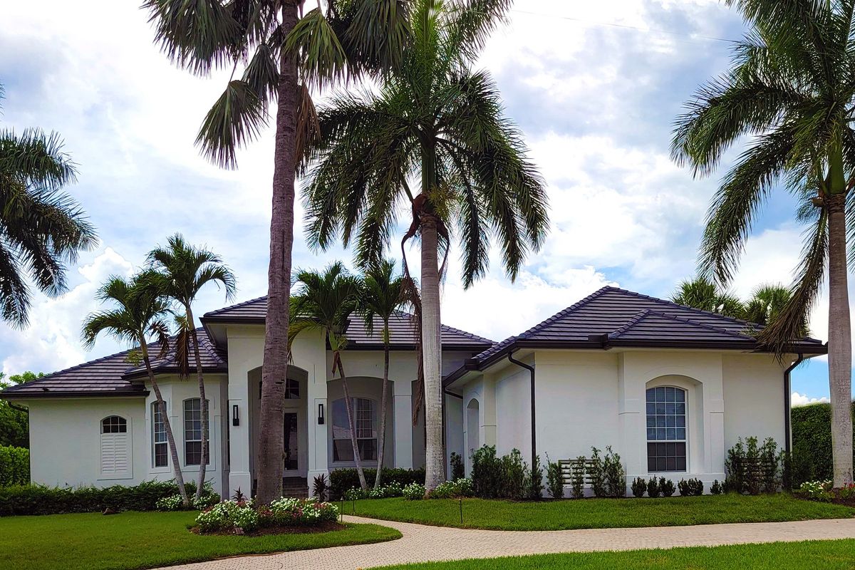 A white single-story house with a tile roof surrounded by palm trees