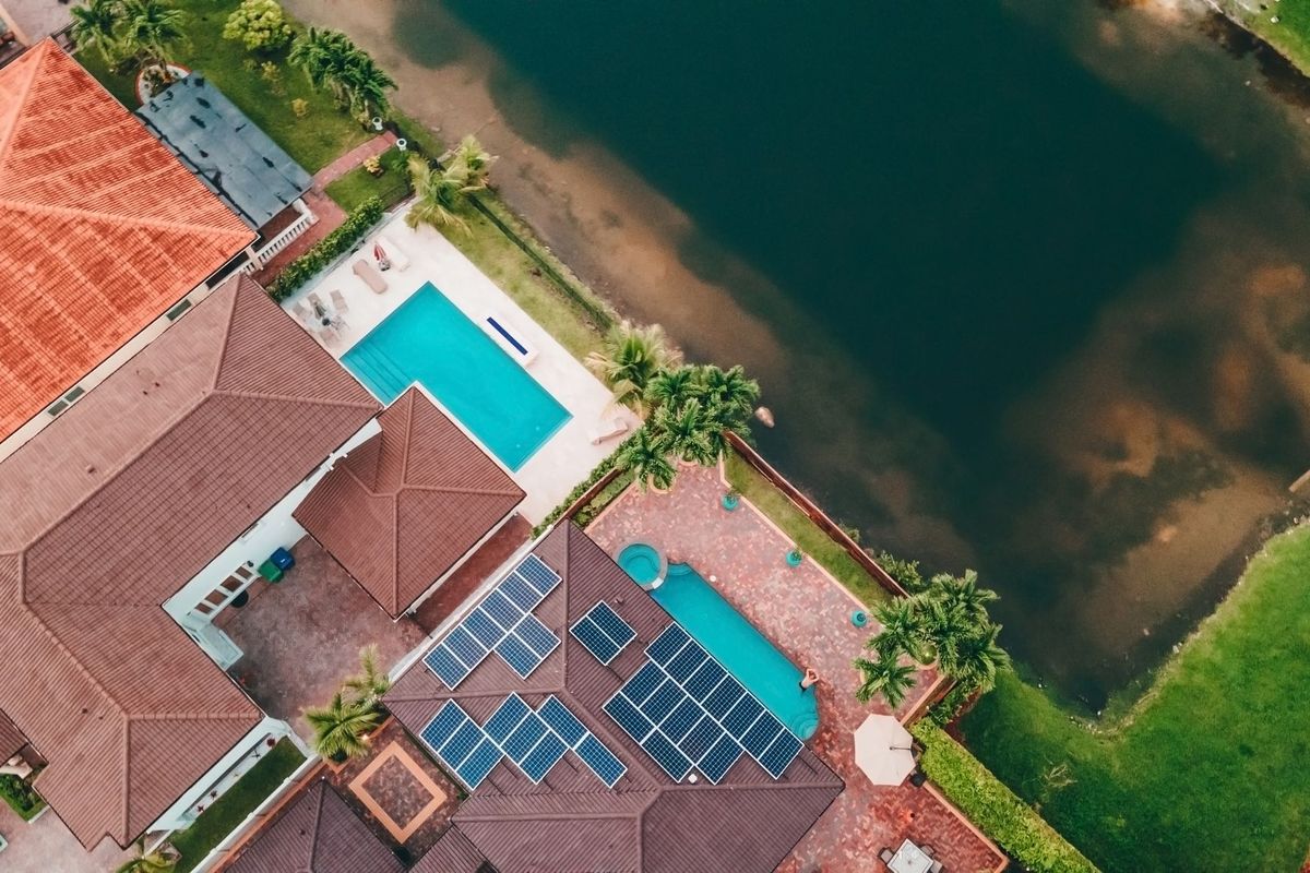 Aerial view of a home with solar panels and a pool next to a lake