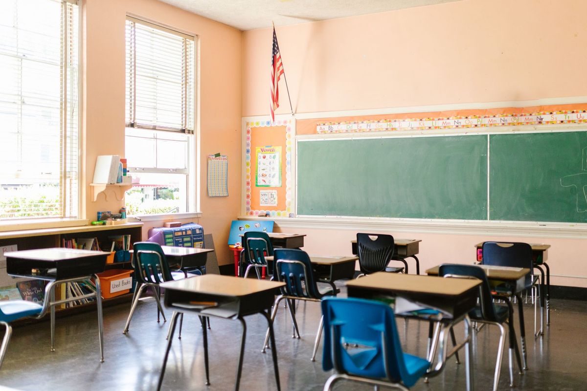 A sunlit classroom with desks, a chalkboard and an American flag